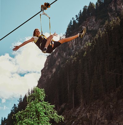Frau genießt Seilrutsche in den Bergen bei sonnigem Wetter