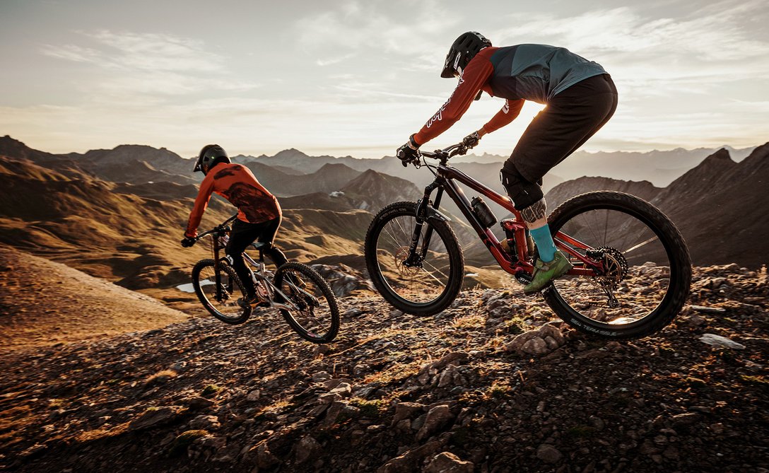 Zwei Mountainbiker fahren einen steinigen Bergpfad bei Sonnenuntergang hinunter