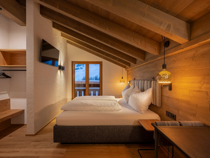 Gemütliches Schlafzimmer mit Holzdecke und Balkonblick auf schneebedeckte Berge