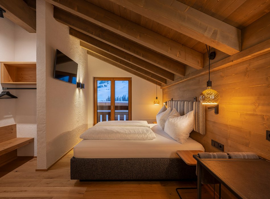 Gemütliches Schlafzimmer mit Holzdecke und Balkonblick auf schneebedeckte Berge