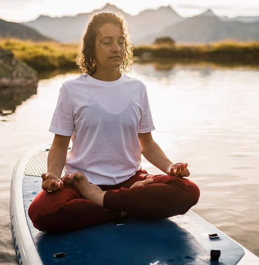 Frau meditiert auf einem Surf-Board auf einem ruhigen Bergsee